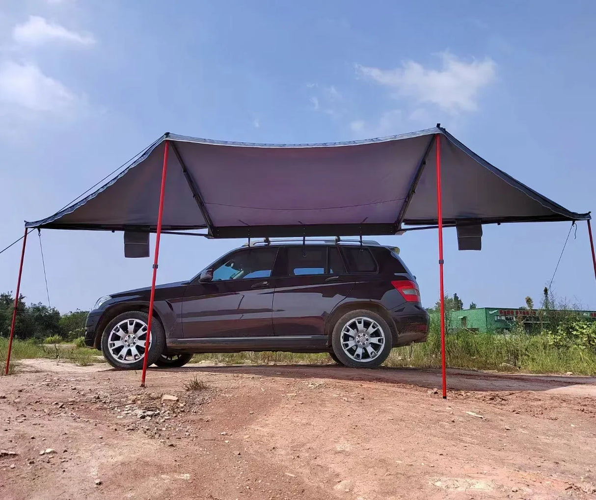 Awning deployed on a dark SUV with red support poles and guy ropes