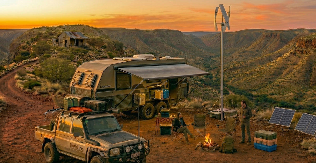 Canyon-top camp at sunset: a vertical wind turbine on a mast beside an off-road caravan, a BushLine ute, solar panels and two people by a campfire