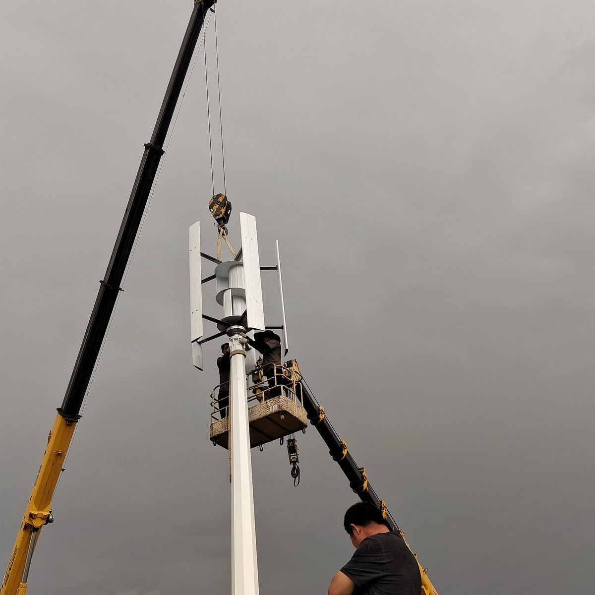 Crane lifting the H1000 rotor onto its mast while installers work from an elevated platform
