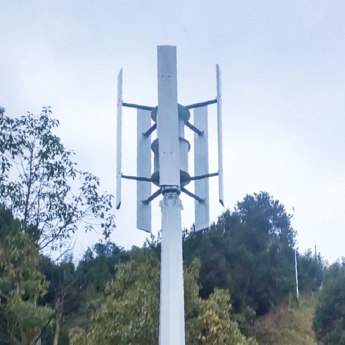 H1000 vertical axis wind turbine installed on a white steel mast among trees