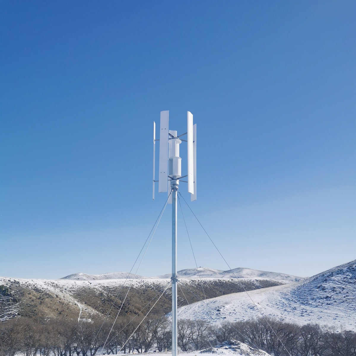H2000 vertical wind turbine on a guyed mast above snow-covered hills