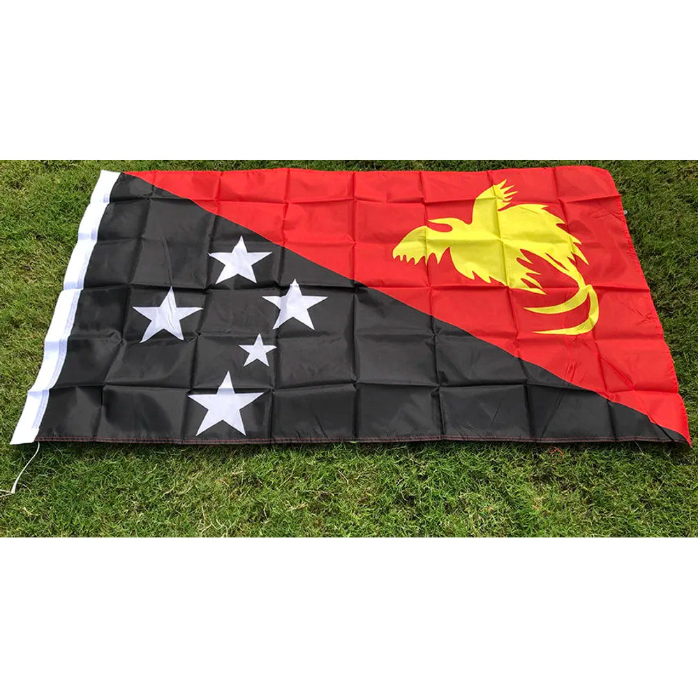 Papua New Guinea flag in printed polyester laid flat on grass: black and red diagonal, white stars, yellow bird of paradise