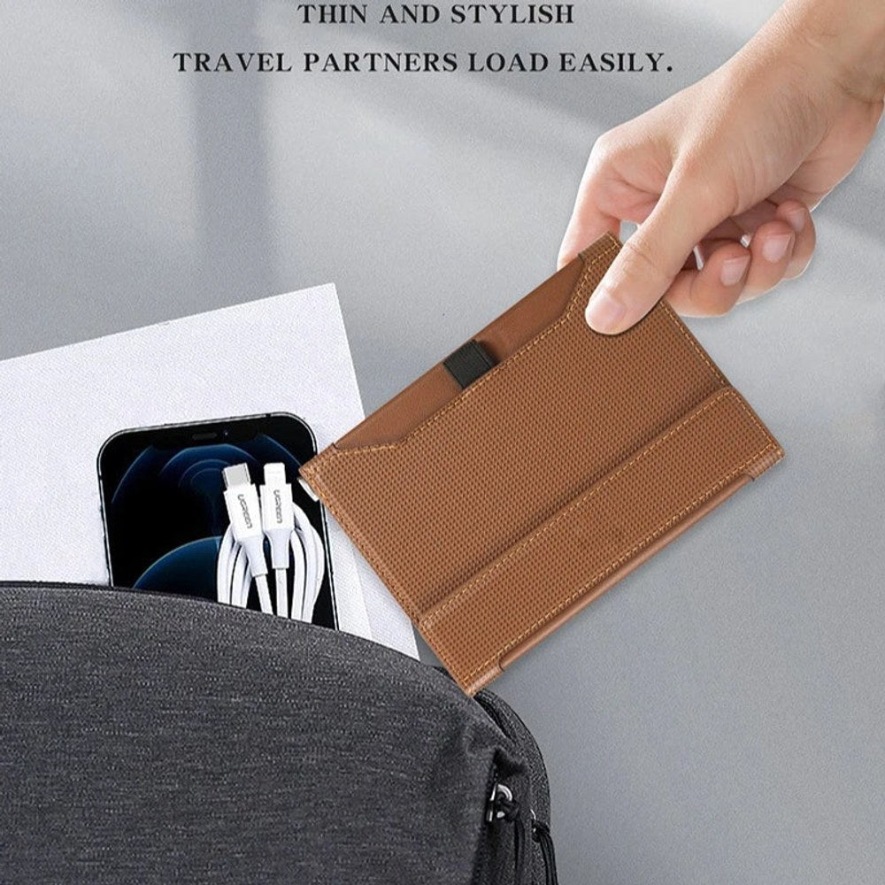 Brown passport holder sliding into the front pocket of a laptop bag beside a phone charger