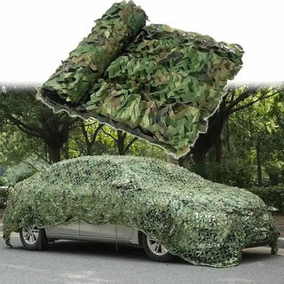 Car partially covered with green camouflage netting in a forest setting