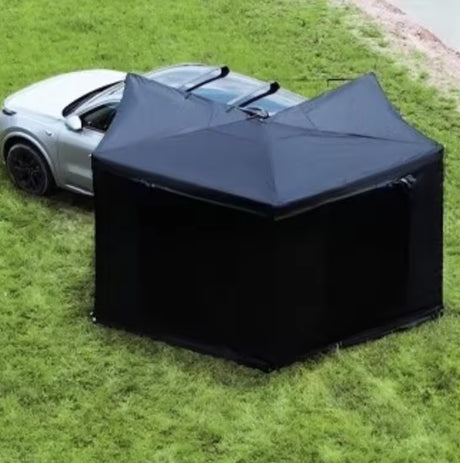 Black awning with full wall kit pitched on grass beside a silver car
