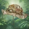 Multi-tone camouflage boonie hat side profile against a blurred green jungle background