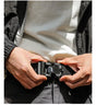 Sunlit shot of both hands fastening the black belt's buckle at the waist over dark trousers