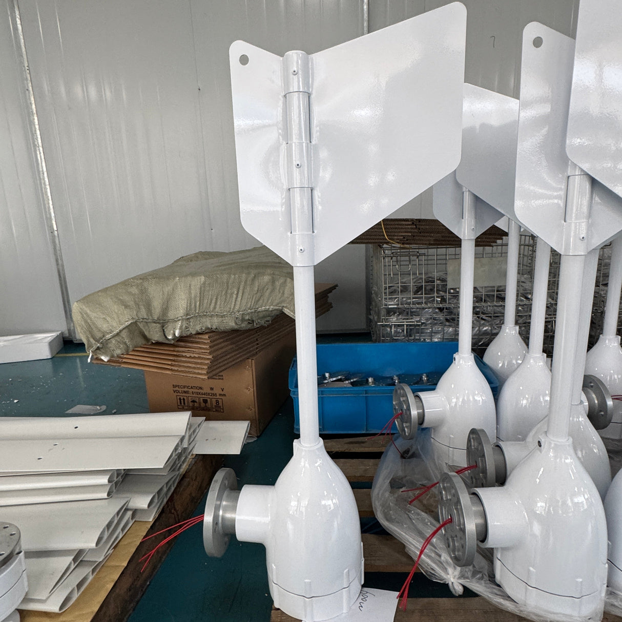 White marine wind turbine blades and hub assemblies stacked on wooden pallets in a warehouse setting.