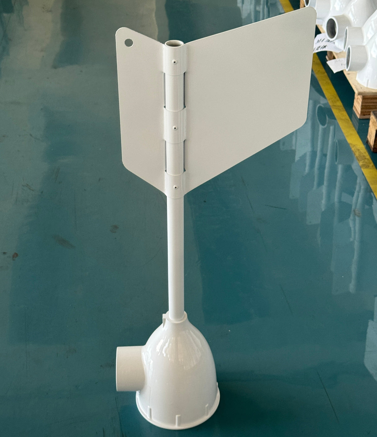 A white marine wind turbine blade assembly with a flared base and hub, standing upright on a blue-gray floor in what appears to be a warehouse or factory setting.