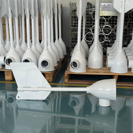 A white marine wind vane and anemole assembly displayed on a warehouse floor, with multiple identical white units stacked on wooden pallets in the background.