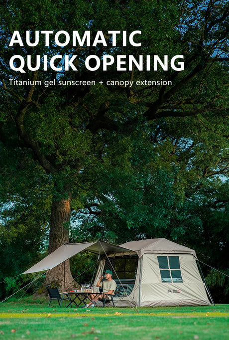 The pitched cabin tent with canopy extended under a large tree, camper seated inside at dusk.