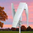 The vertical turbine at dusk beside an autumn tree, blades still against a pink and mauve sky.