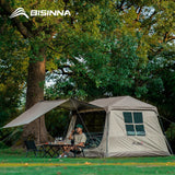 Sand BISINNA cabin tent pitched under a tree with the canopy extended, camper seated at a table.