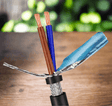 Two-core shielded cable on a timber bench, brown and blue cores exposed above the foil wrap and braided screen.