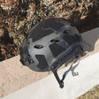 Top-down view of the black multicam helmet on a kerb, showing the crown vents and the hook-and-loop panels across the top