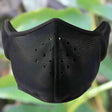 Black half face mask with punched ventilation holes across the mouth panel, leafy background