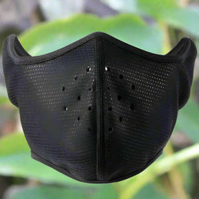 Black half face mask with punched ventilation holes across the mouth panel, leafy background