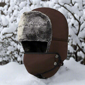 Brown trapper hat side on, grey pile lining showing, face panel fitted, snowy branches