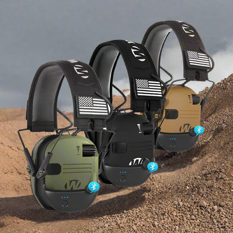 Three electronic ear muffs — olive green, black and tan — lined up on a dirt mound outdoors