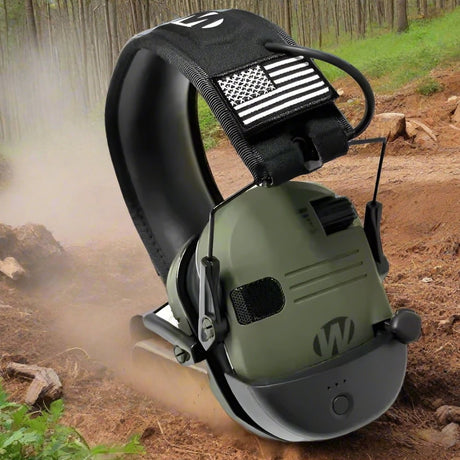 Olive green ear muff on a dusty forest track, showing the vent grille and three battery LEDs