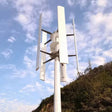 Five-blade H12 H-type vertical axis wind turbine on a guyed pole mast above a coastal hillside - representative family photo