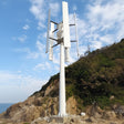 Five-blade H12 H-type vertical axis wind turbine on a guyed pole mast above a coastal hillside - representative family photo