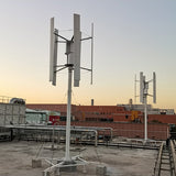 Two five-blade H12 vertical axis wind turbines on braced masts at an industrial site at sunset - representative family photo