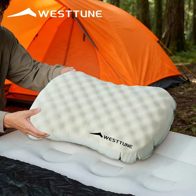 Off-white inflatable camping pillow being placed on a sleeping mat in a tent