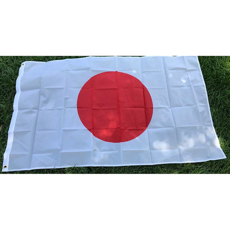 Japanese flag in printed polyester laid flat on grass: red disc on white, white header strip at left
