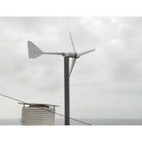 L-series wind turbine pole-mounted beside a weather station enclosure on an ocean-front deck under a grey sky - representative family photo