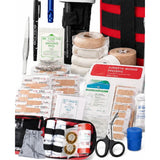 First aid bag opened flat with rolled bandages and tape strapped inside, next to plasters, wound pads, safety pins, tweezers, a marker pen, a whistle and trauma scissors