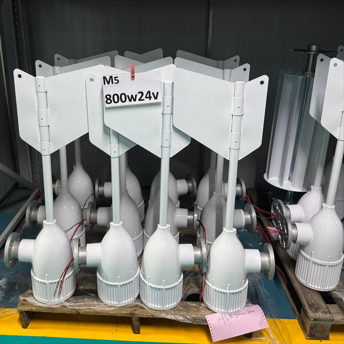 Finned generator bodies with tail vanes and booms fitted, palletised at the factory under a label reading M5 800w24v.