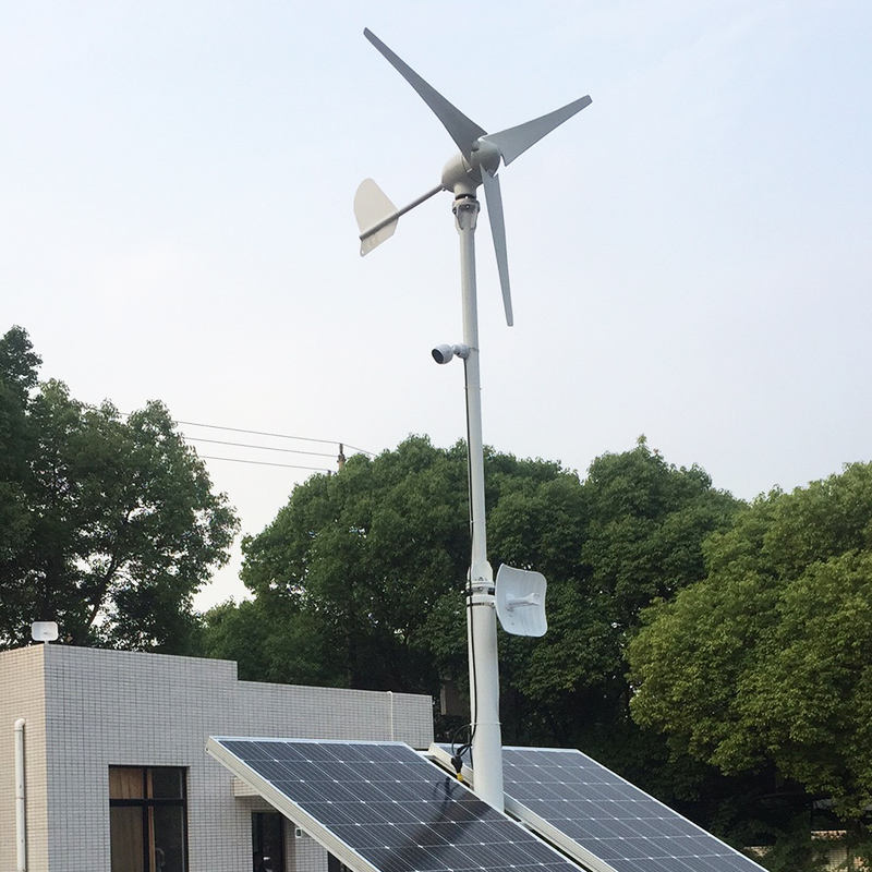 M-series turbine above two solar panels on a rooftop pole mount with CCTV camera and antennas - a wind-solar hybrid setup