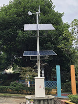 Wind-solar street pole in a park: a small horizontal turbine on top, two tiers of solar panels, LED street lamp and control cabinet on a concrete plinth