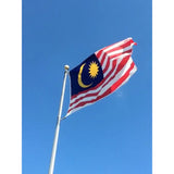 Malaysian flag in printed polyester flying from a pole against blue sky: red and white stripes, crescent and star on blue