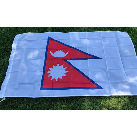 Nepal flag in printed polyester laid flat on grass: two red pennants with moon and sun, printed on a white rectangle