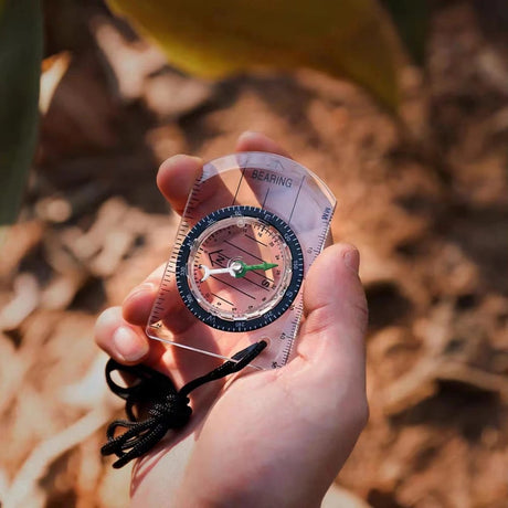 Clear baseplate compass with a degree dial and black cord lanyard held in an open hand