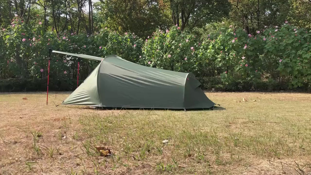 Green two-person tent pitched on dry grass, filmed in a slow walk-round, including the porch flap held up on red poles.