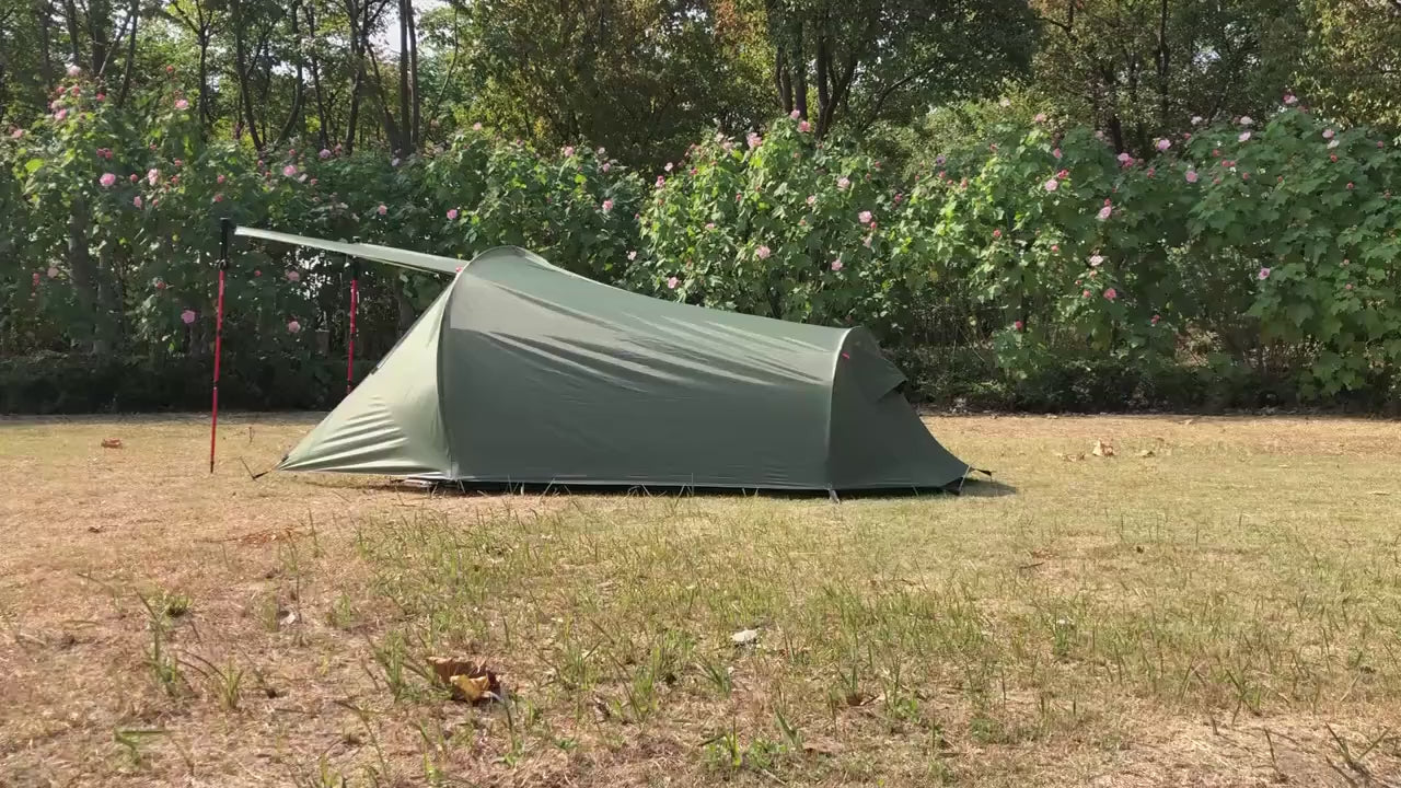Green two-person tent pitched on dry grass, filmed in a slow walk-round, including the porch flap held up on red poles.