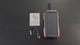 Black and orange rugged solar power bank up close: the solar panel face, the end torch switched on, the four charge lights and the ports, then charging a tablet and a phone at the same time.