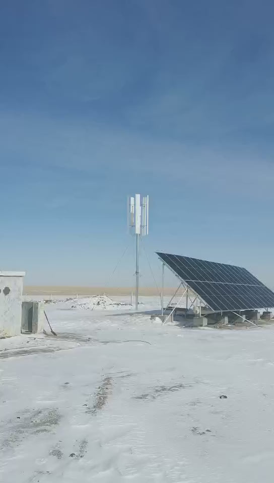 H2000 vertical wind turbine turning on its mast beside a solar array on a snowy plain