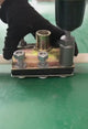 A long hex socket in a cordless drill, spinning nuts off the bolts of a clamp bracket on a workbench.