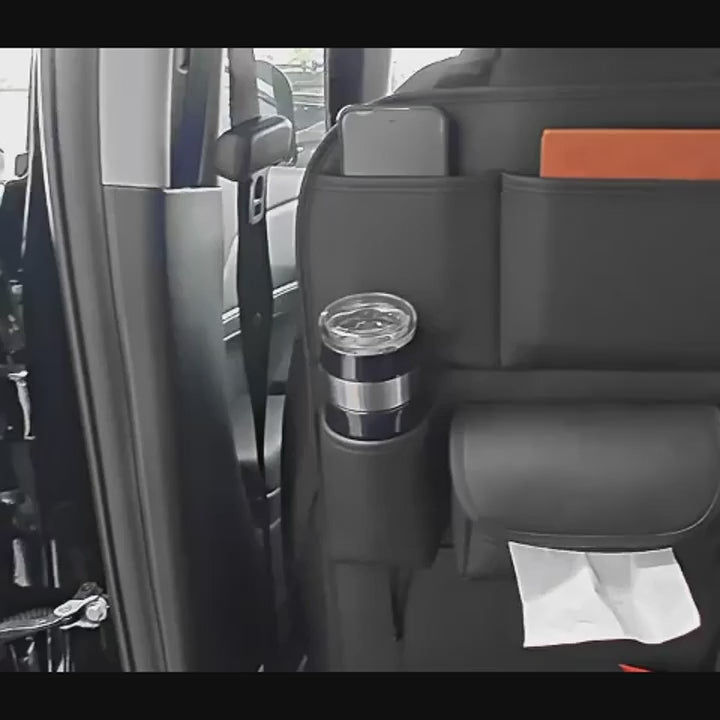 The black seat-back organiser on a car seat with a bottle, tumbler and tissues, then hung over the front seat, strapped under the bottom edge and filled with a tablet, phone and drinks.