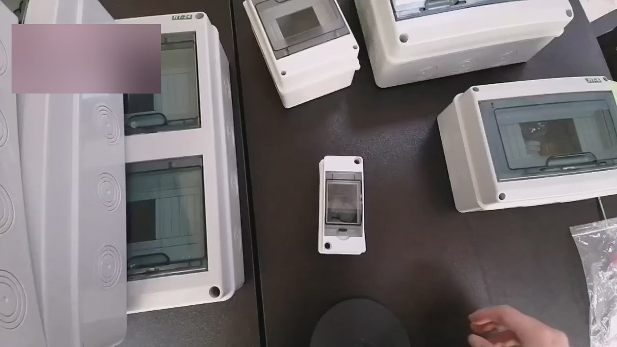 Hands open several grey IP65 junction boxes on a bench to show the clear covers, the DIN rail inside and the seals.