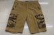 Khaki cargo shorts laid flat while hands open the flap pockets on the thighs, side seams and seat, showing the camo pocket facings.