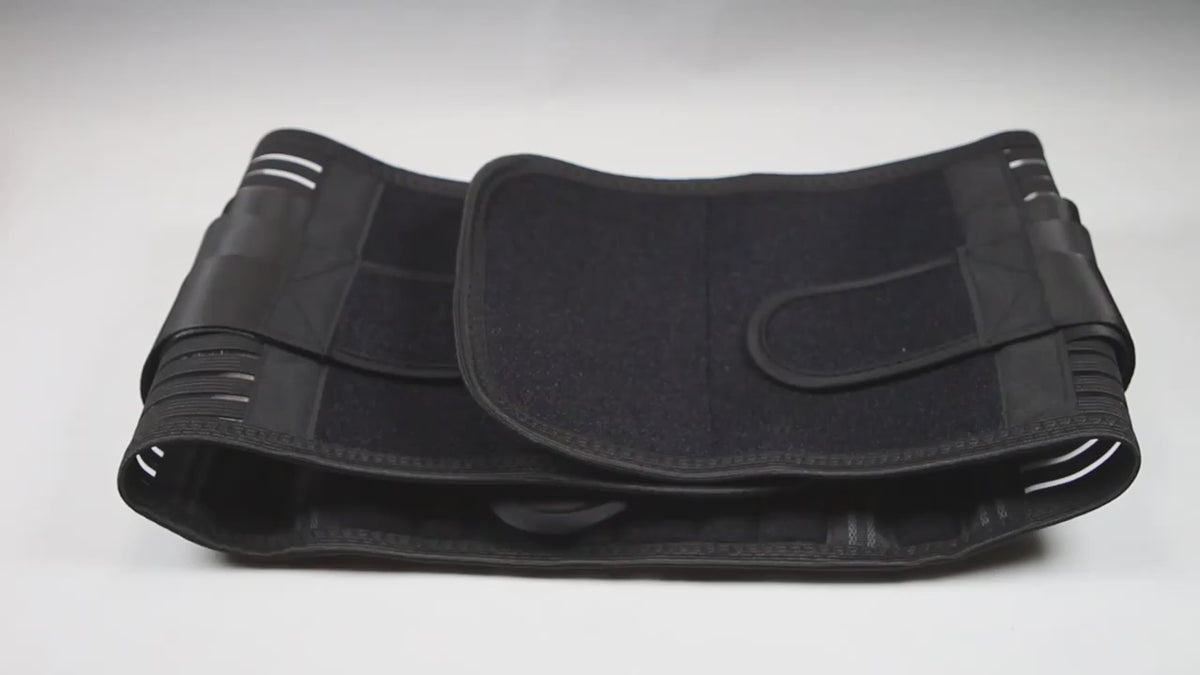 Hands showing the black lumbar support belt: the wide back panel with its stays, the double-pull elastic straps being stretched and the moulded back pad fitted into the panel.