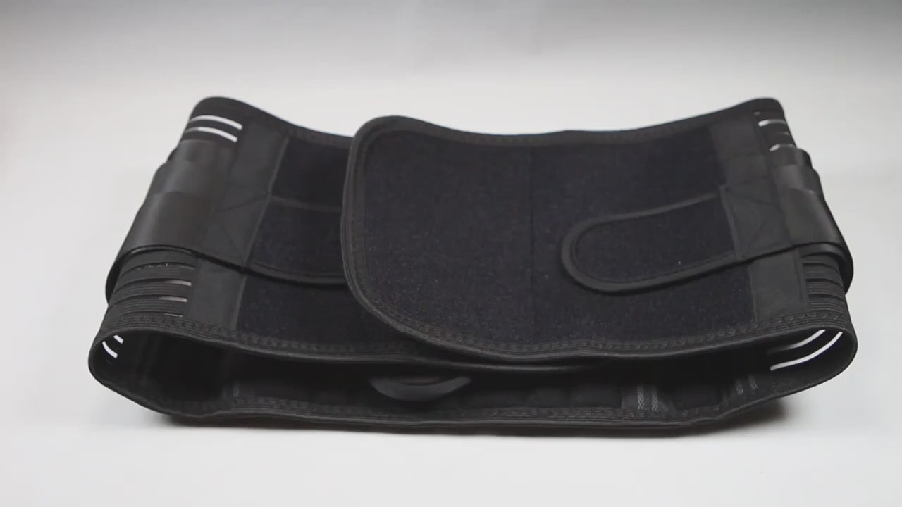 Hands showing the black lumbar support belt: the wide back panel with its stays, the double-pull elastic straps being stretched and the moulded back pad fitted into the panel.
