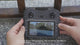 XT606 screen remote held in two hands, its screen showing the camera picture and the menu as the buttons are pressed.