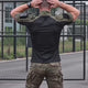 A man in a black combat shirt with olive green shoulders and sleeves turns from back to front, stretching his arms out and then folding them.