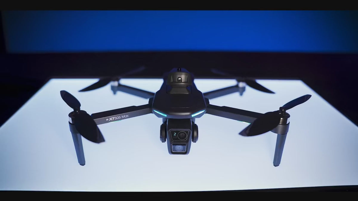 XT606 drone on a lit stand, then flying over farmland, cloud and forest; its screen remote on a rock and in hand showing the live picture; close-ups of the camera, a motor and the camera wheel; ending with the remote and the folded drone side by side on grass.